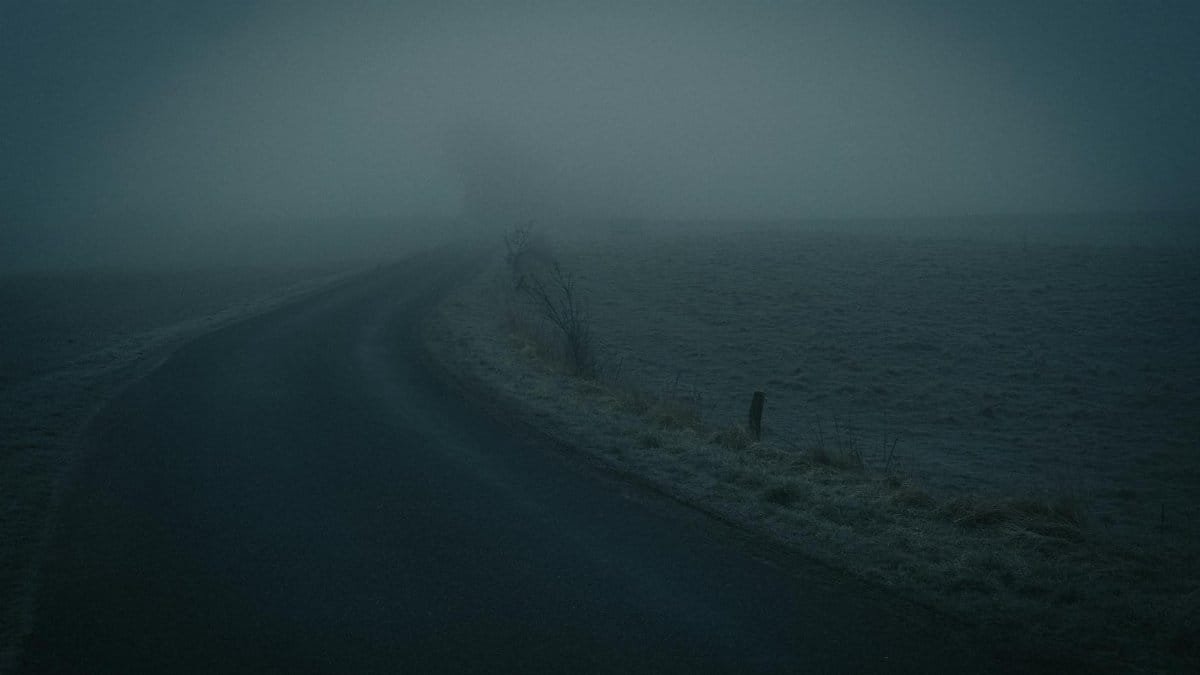 A dark, foggy road in the countryside creates an eerie and mysterious atmosphere.
