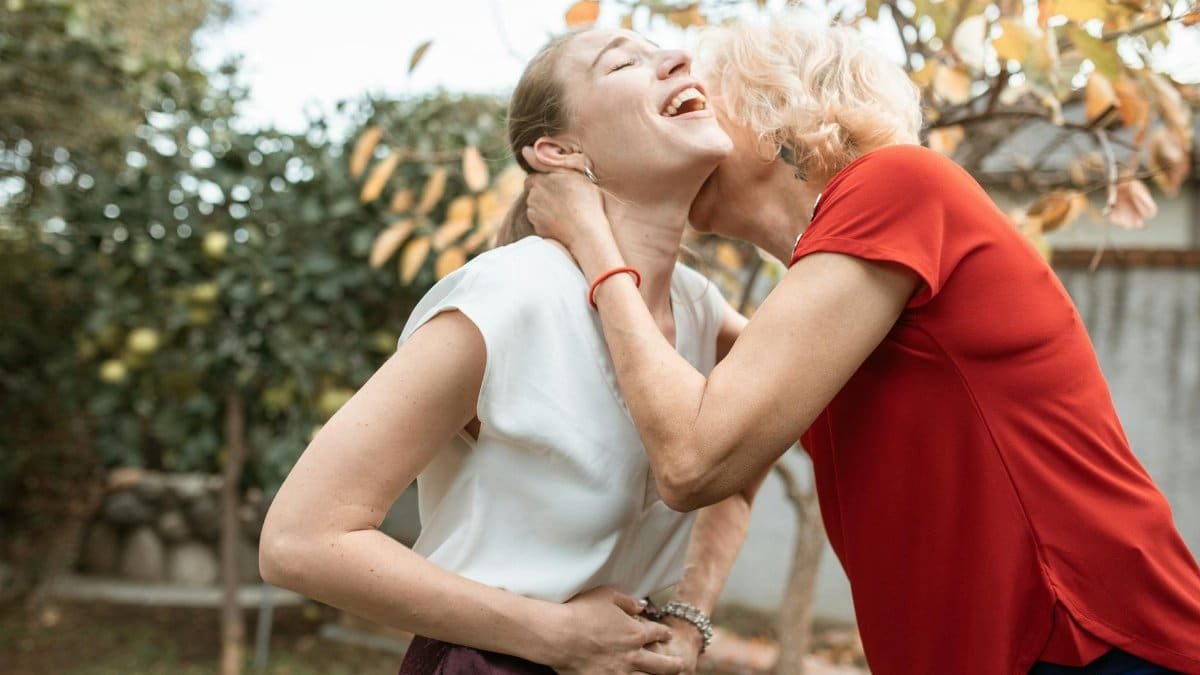 Elderly woman joyfully embraces a younger woman in a sunny garden setting.
