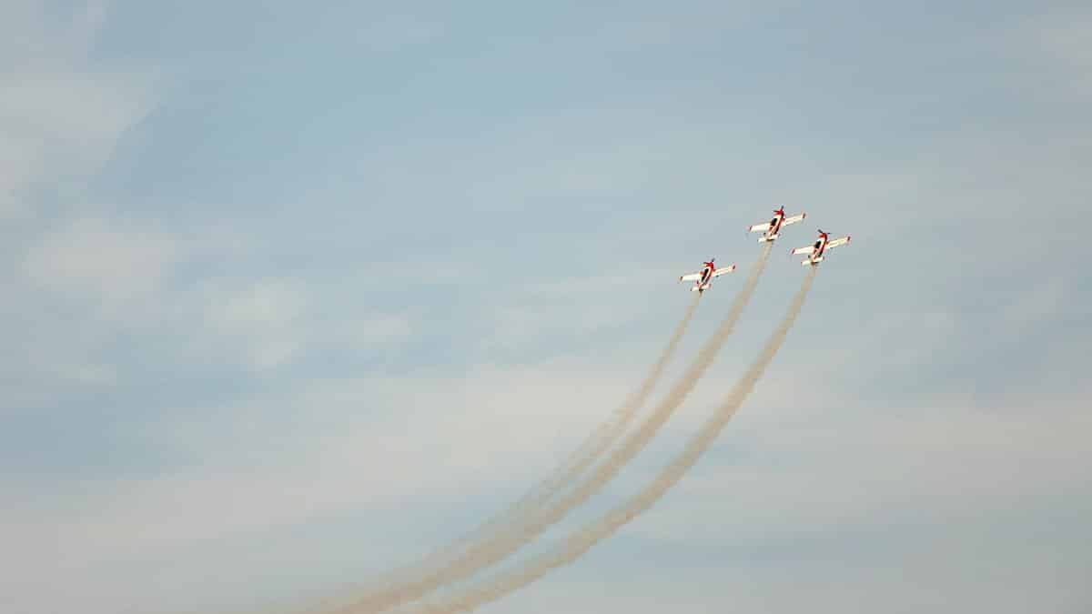 Three stunt planes performing a formation flight against a clear blue sky, leaving smoke trails.