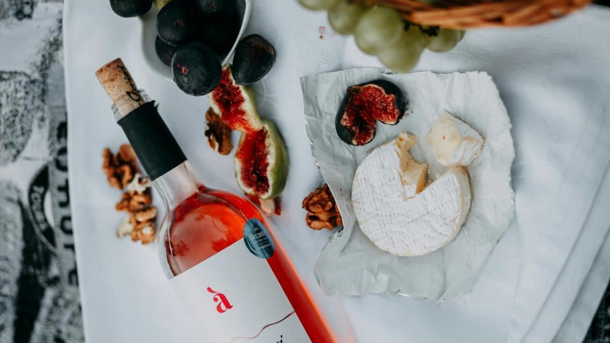 A sophisticated picnic setup featuring wine, cheese, figs, and walnuts on a white cloth.