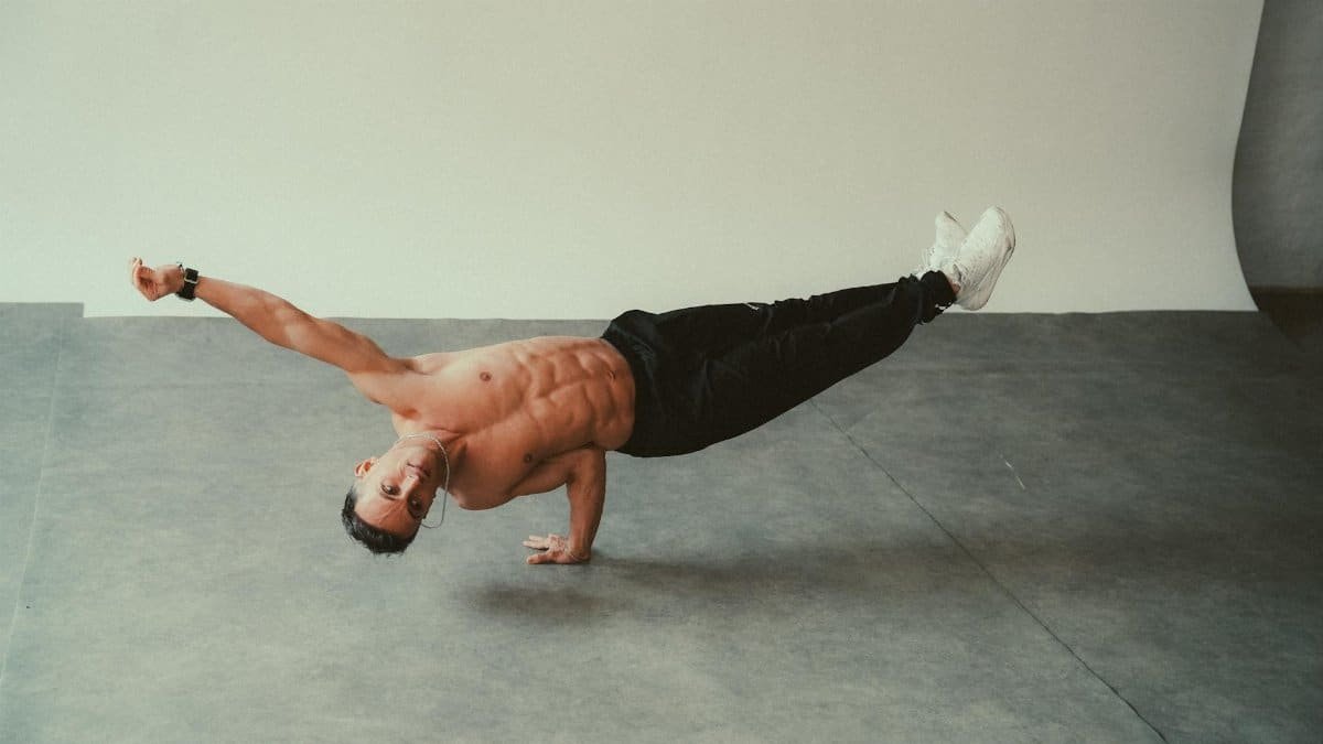 Man performing a one-arm balance exercise indoors, demonstrating fitness and strength.
