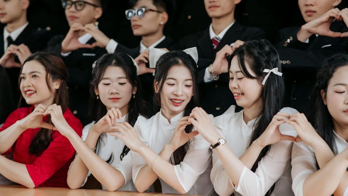 Happy group of young adults forming heart shapes with hands, showcasing unity and friendship.