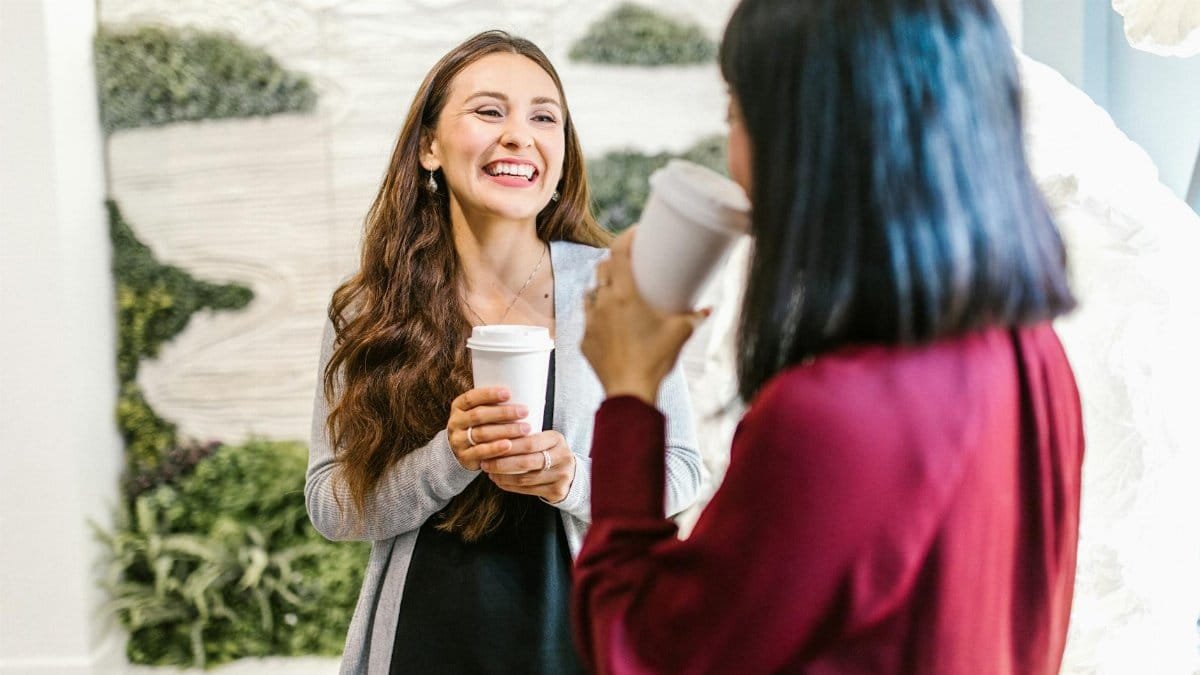 Two women in a modern office setting enjoying a casual coffee break, highlighting teamwork and relaxation.