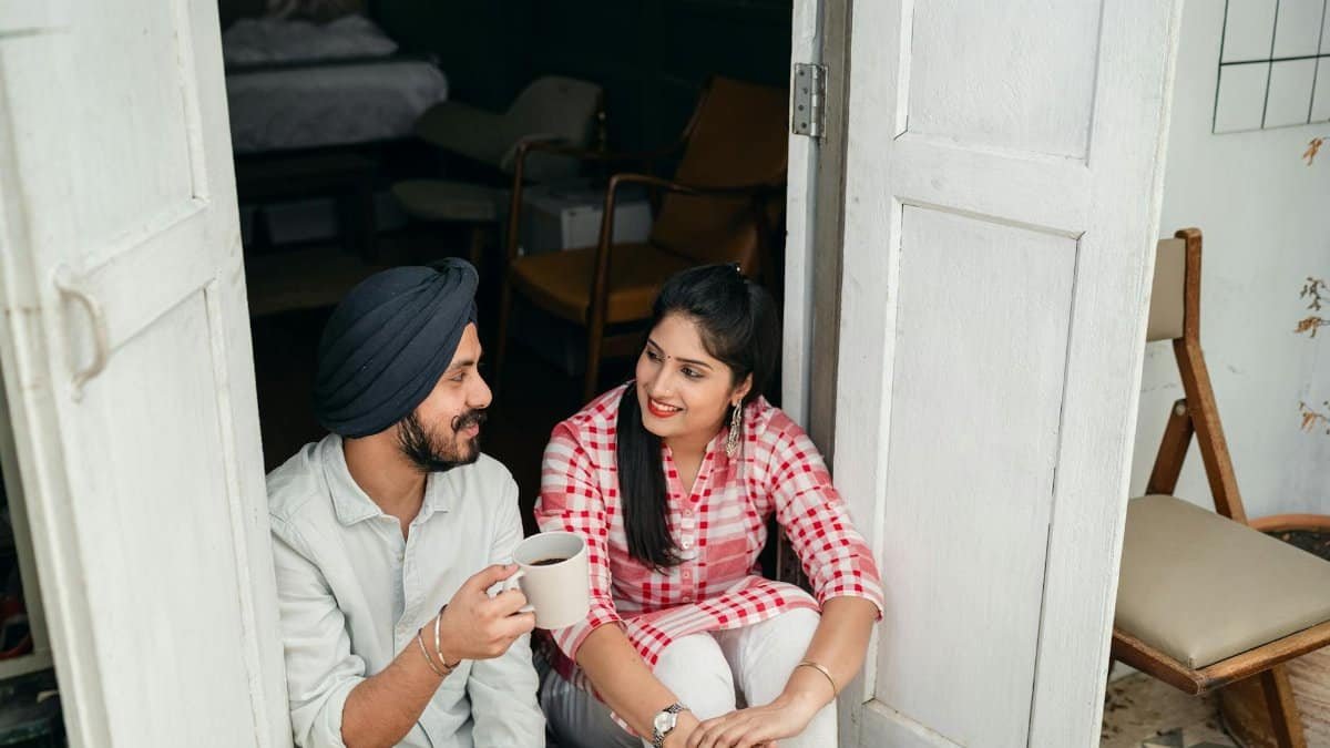 A happy couple sits in the doorway enjoying their morning coffee, smiling and conversing.