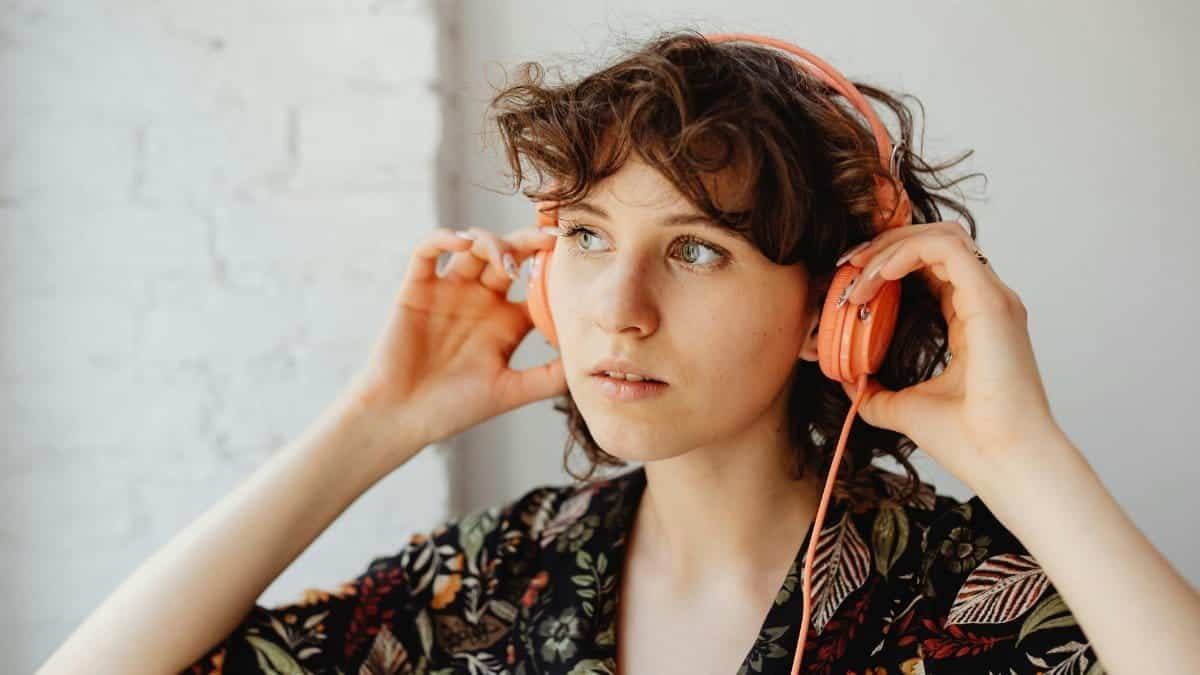 A woman wearing headphones and a floral shirt listens to music indoors.