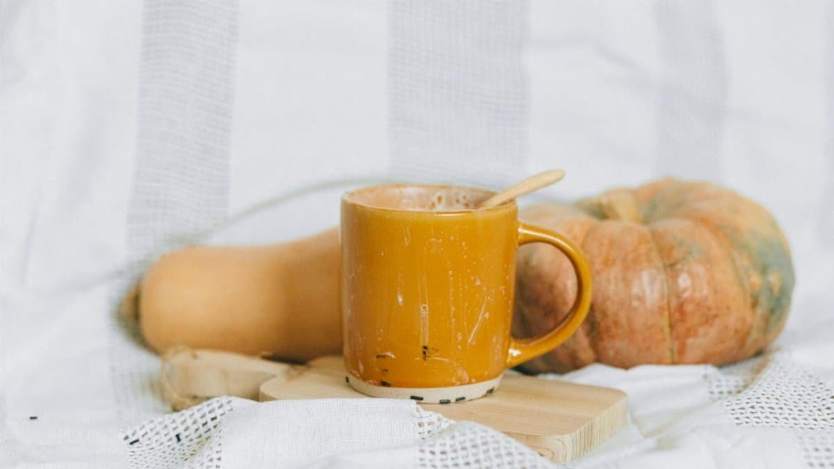 Warm autumn drink in a yellow mug with pumpkin and squash on a soft background.