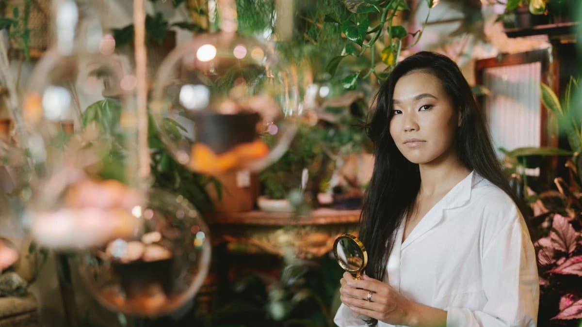 Female botanist examining plants with magnifying glass in a lush indoor setting.