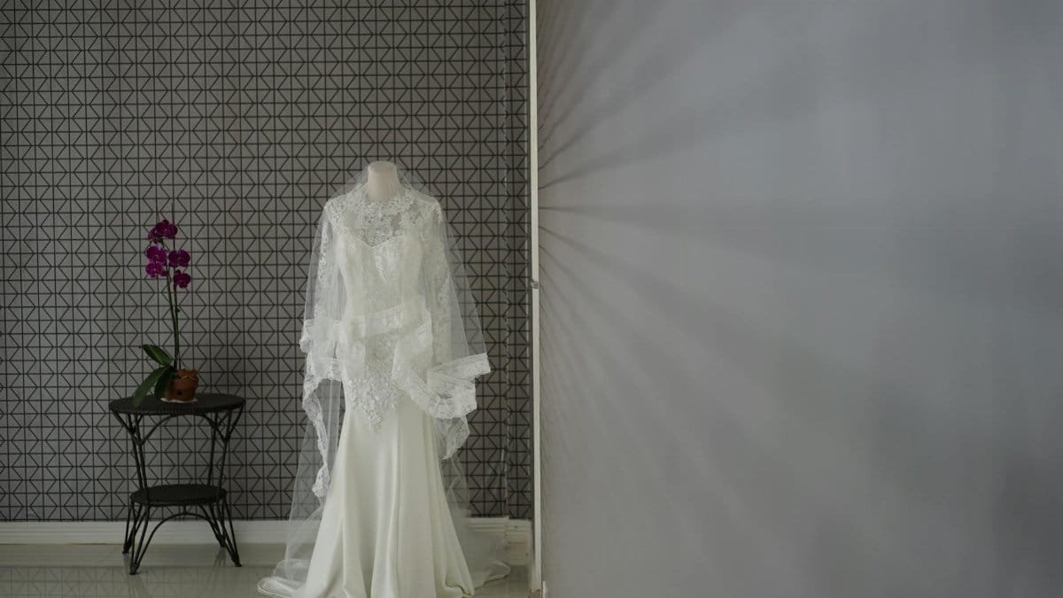 A bridal mannequin displaying a wedding gown with a lace veil, next to a table with pink orchids.