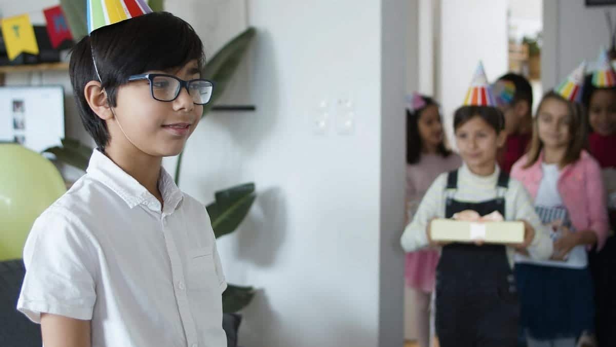 Children celebrating a birthday party indoors with gifts and party hats.