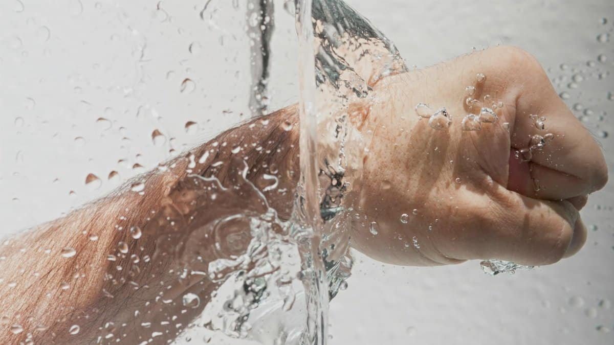 Dynamic image showing a clenched hand submerged in a splash of clear water, emphasizing motion and hygiene.