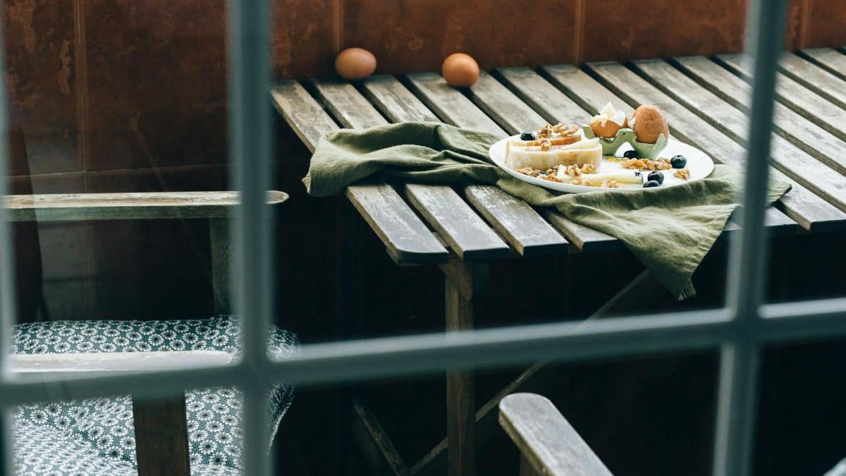 Cozy rustic breakfast with bread, cheese, and eggs on a wooden table as seen through a window.