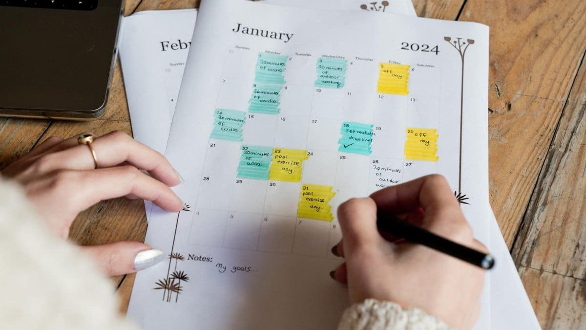 A woman marking events on a January 2024 calendar with colorful notes, focusing on planning.