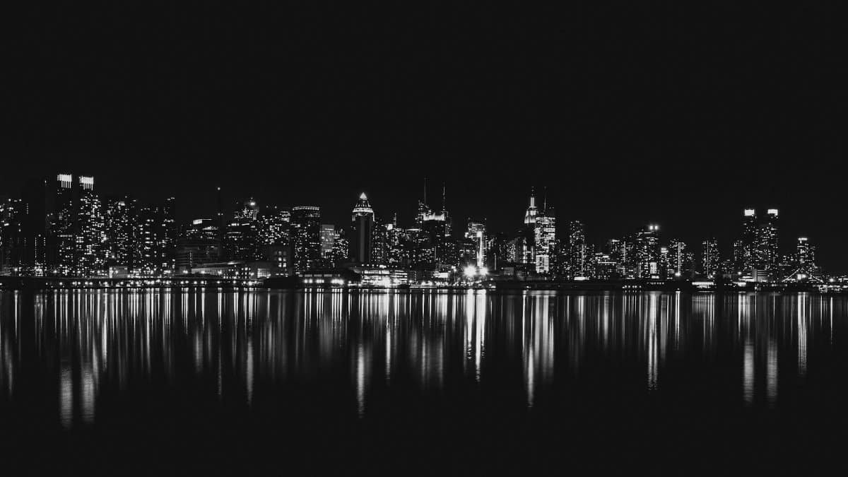 Captivating black and white view of New York City skyline reflecting on water at night.