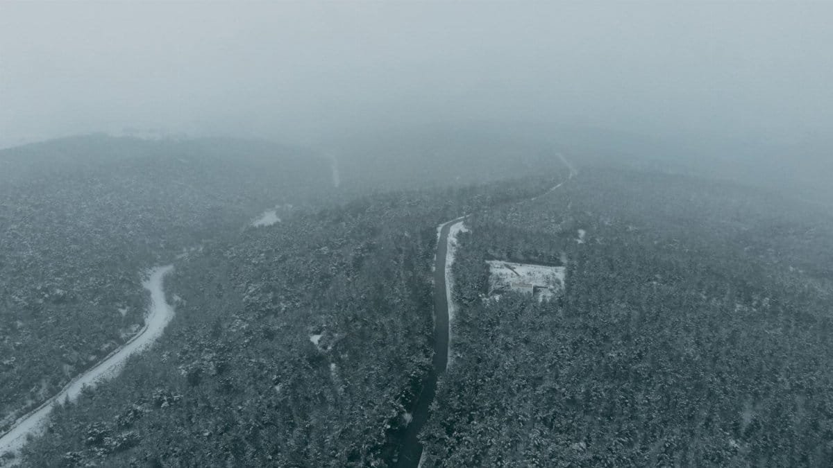 Aerial view capturing a foggy winter forest landscape in Hacıkadem, Uşak, Turkey, featuring snow-covered trees and a curving road.