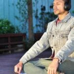 Adult man practicing meditation and relaxation with headphones in a serene outdoor setting.