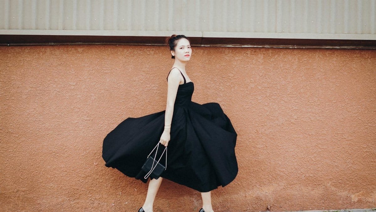 Stylish woman in black dress and heels walking confidently by a brick wall, showcasing elegance.