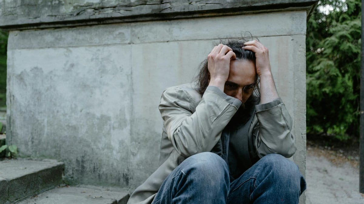 A pensive man sits on stone steps outdoors, embodying feelings of worry and sadness.