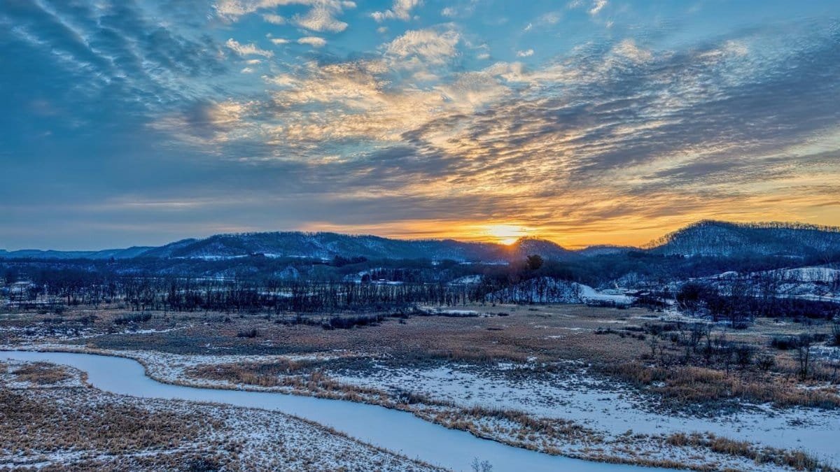 A beautiful winter sunset over a snowy landscape in Tell, Wisconsin, USA, with a winding stream and mountains.