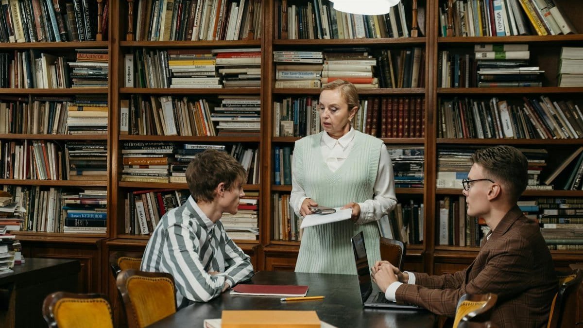 A librarian engages in a discussion with students in a library filled with books.