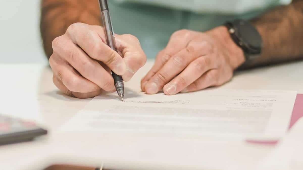 Close-up of a man signing an official document with a ballpoint pen on a desk.