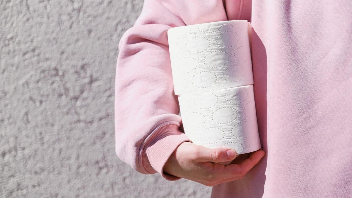 Close-up of a person in a pink sweater holding two toilet paper rolls outdoors.