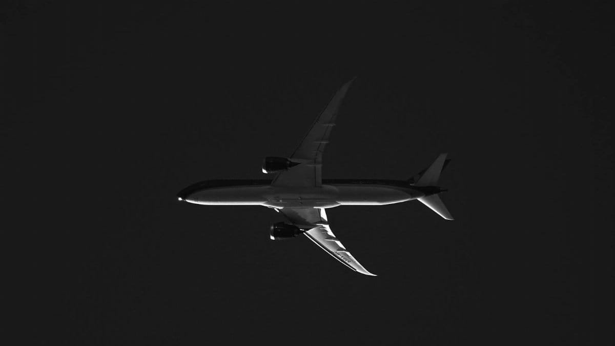 A striking black and white silhouette showing an airplane soaring high in the sky.