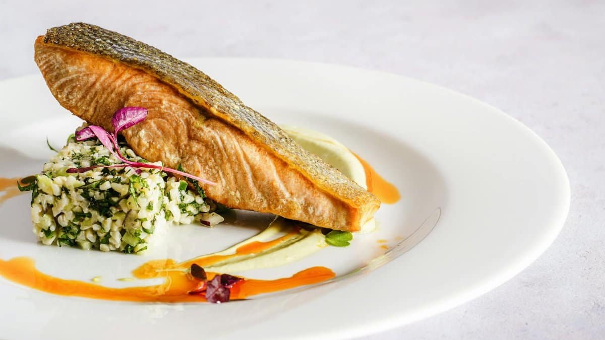 A beautifully plated salmon dish with quinoa, herbs, and a vibrant sauce, perfect for gourmet food lovers.