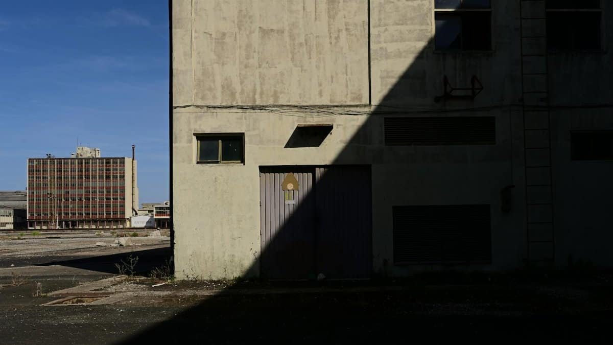 A shadow casts over an empty industrial building exterior in an abandoned area.