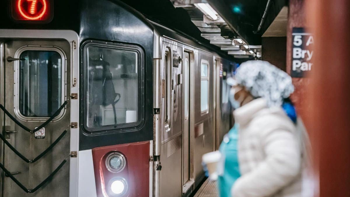 Unrecognisable female in medical uniform coat and with paper cup waiting for train arriving on subway platform