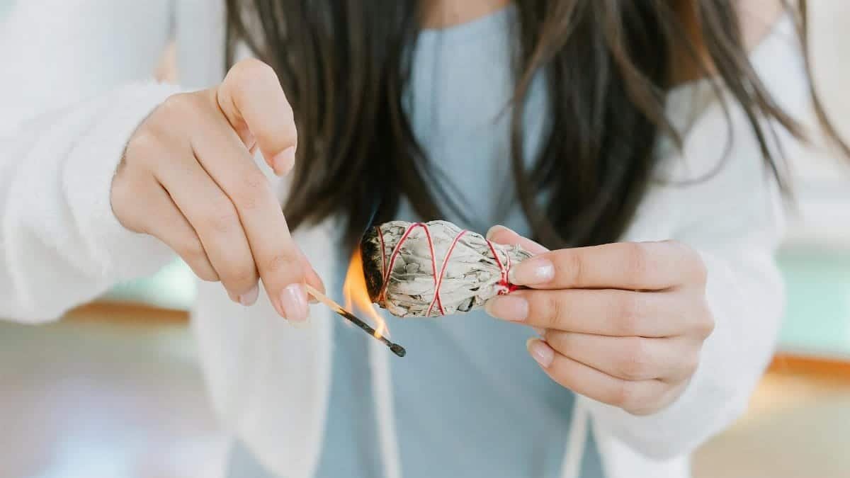 A woman burning sage for a cleansing ritual indoors, promoting tranquility and spiritual healing.
