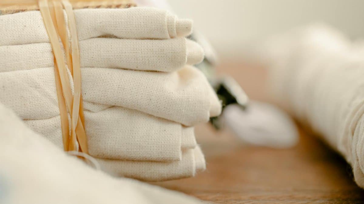 A pile of neatly folded organic cotton textiles tied with rope on a wooden table.