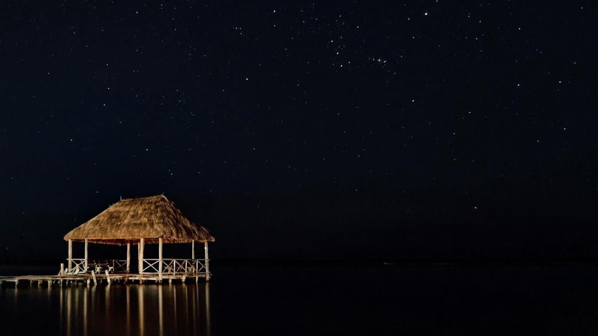 Serene night scene of a gazebo reflected in calm waters under a starlit sky in Bacalar, Mexico.