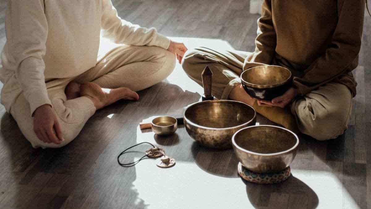 Two women meditating with Tibetan singing bowls in a serene indoor setting.
