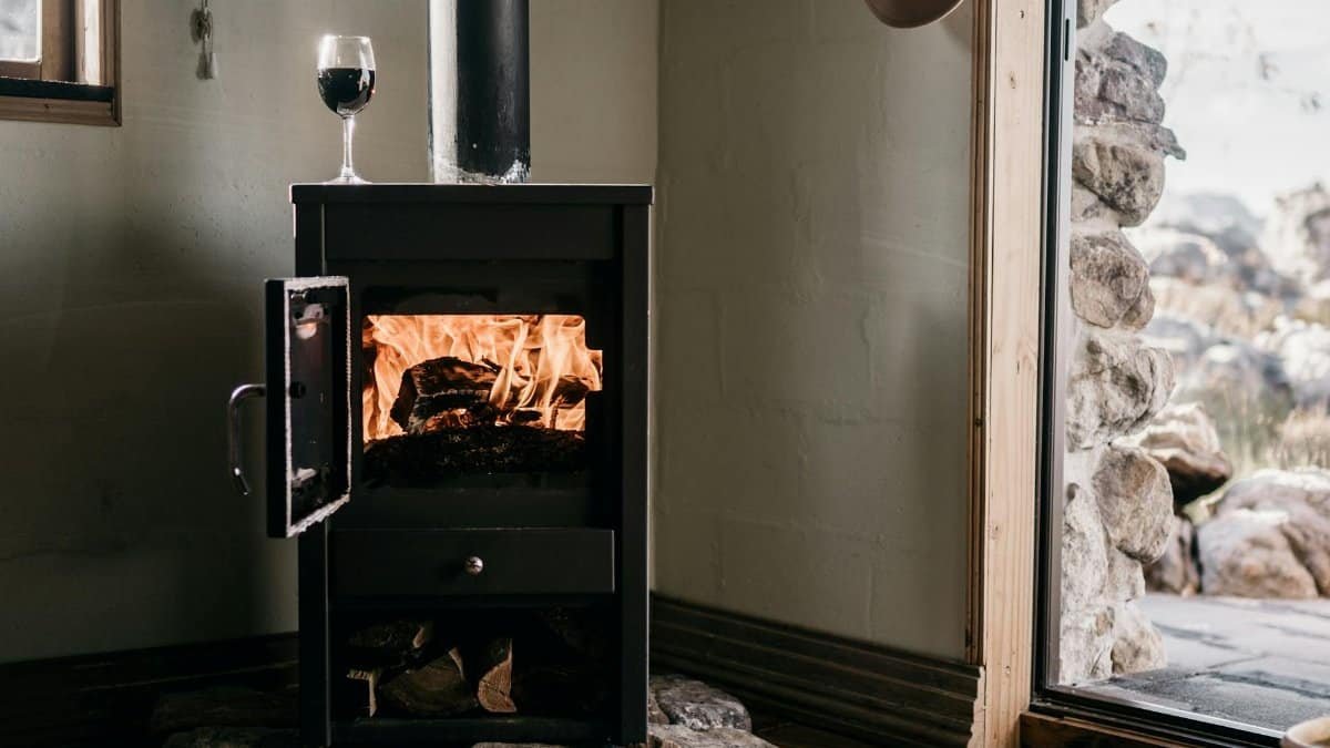 Warm indoor scene with a wood stove burning firewood beside an open door and glass of wine.
