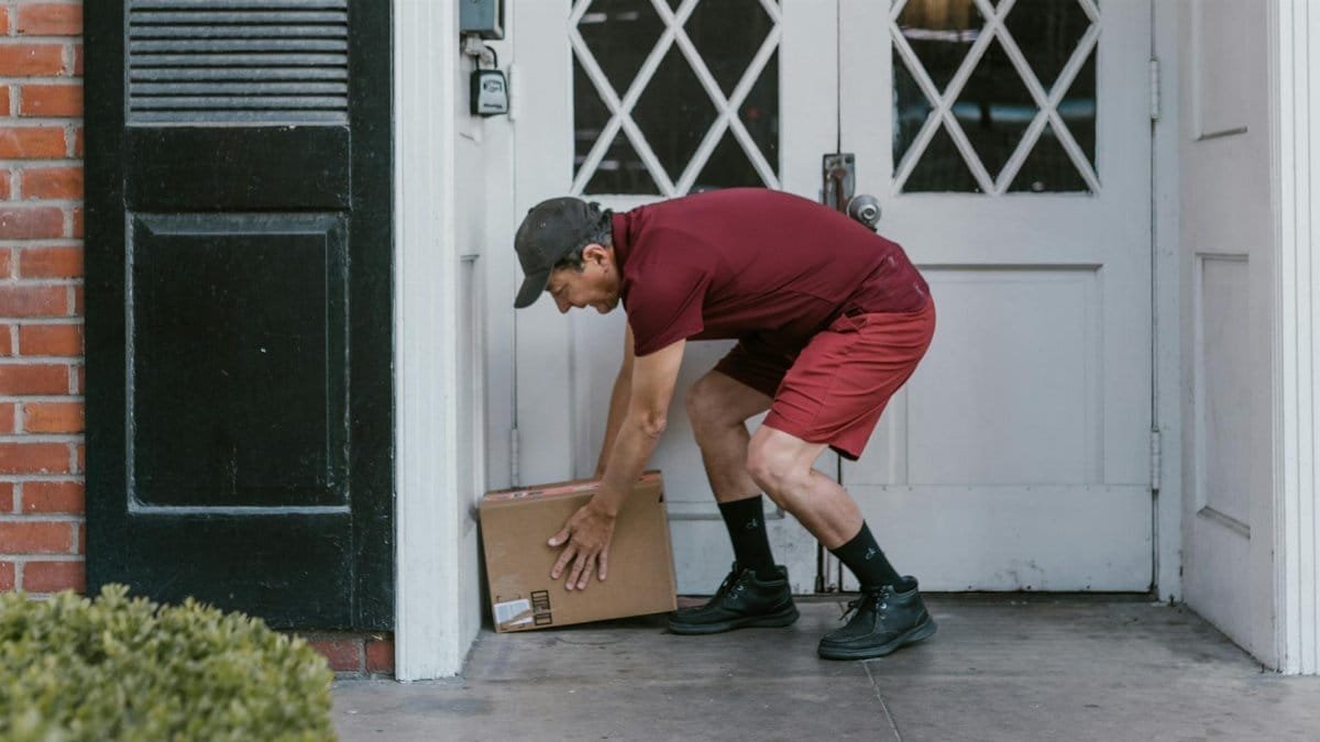Delivery person in red uniform leaving a package at a home's front door.