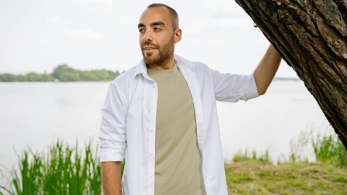 A man enjoying a serene moment by the river, leaning on a tree and smiling.