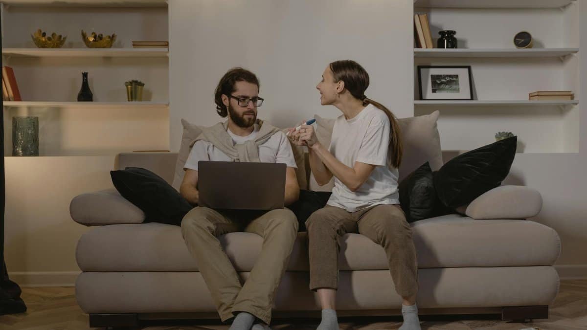 Happy couple sitting on couch, celebrating pregnancy news with test results.