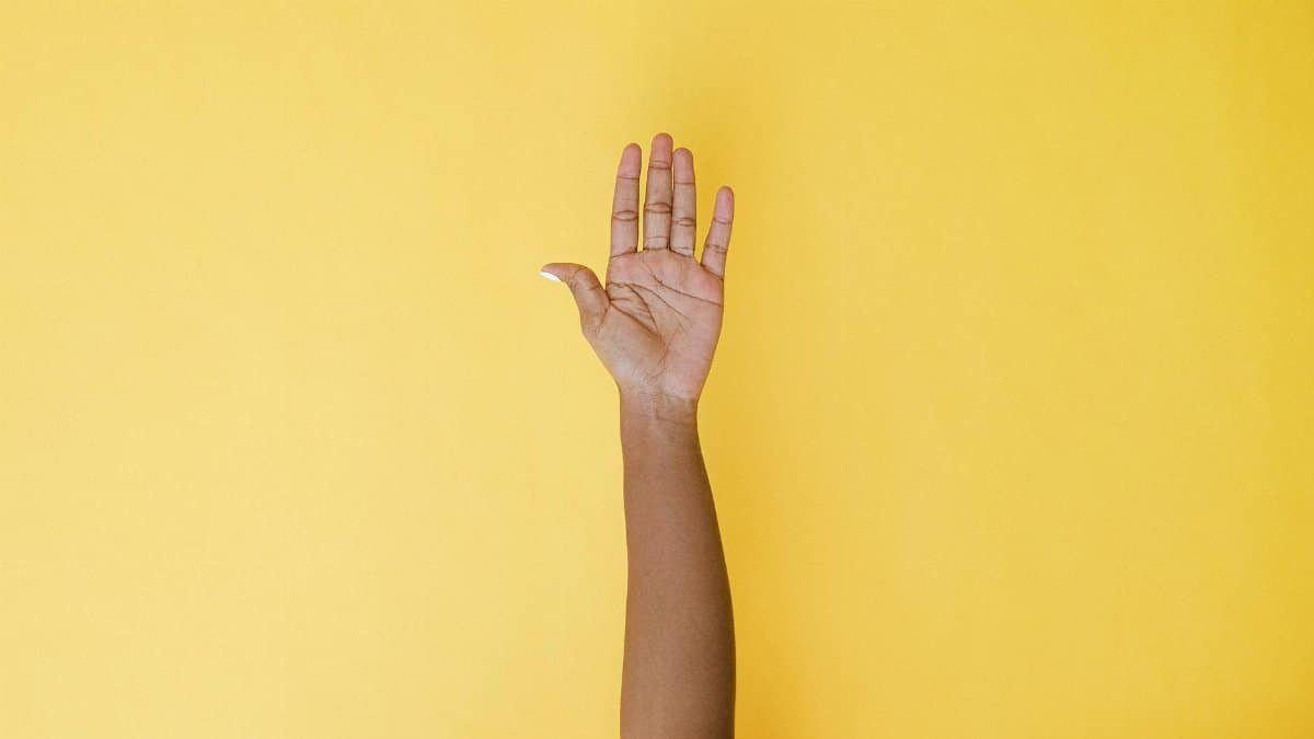 A hand raised against a vibrant yellow background, symbolizing help or volunteering.