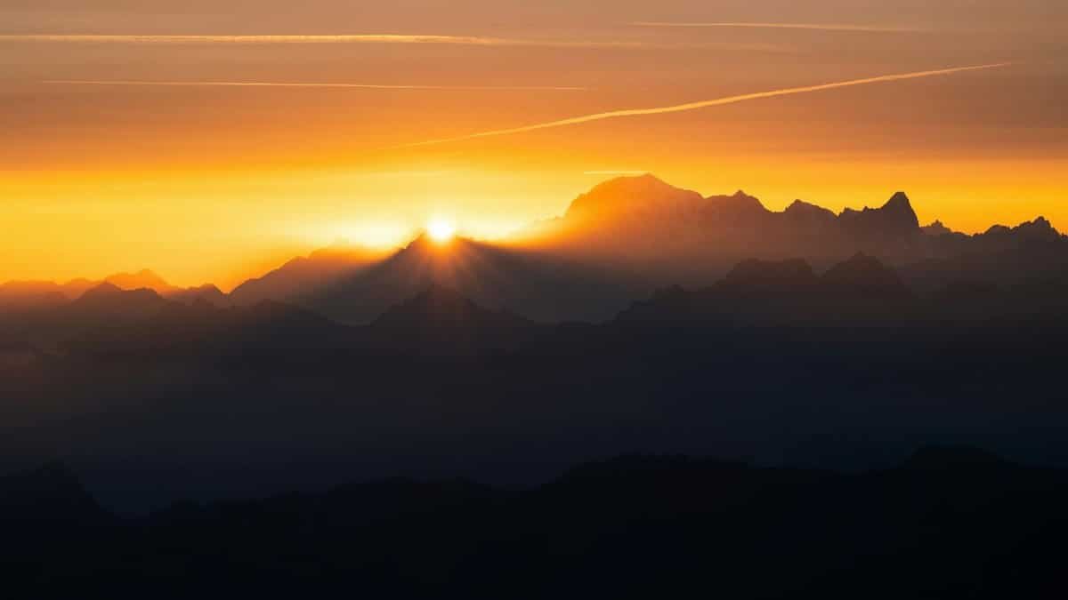 A breathtaking view of the sun setting over the rugged mountain peaks, casting a warm glow.