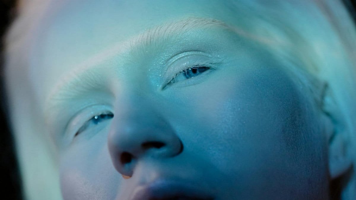 Close-up shot of an albino individual with blue lighting creating a serene and unique visual effect.