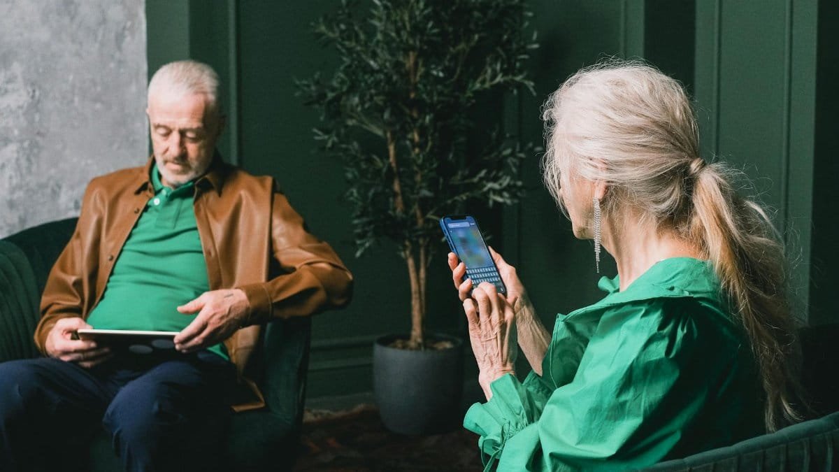Elderly couple using digital devices in modern green living room, highlighting technology engagement.