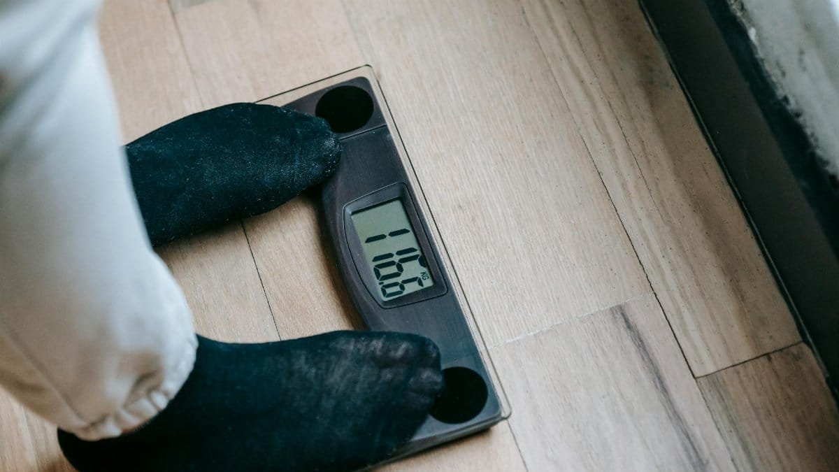 From above of unrecognizable person in socks standing on electronic weighing scales while checking weight on parquet during weight loss