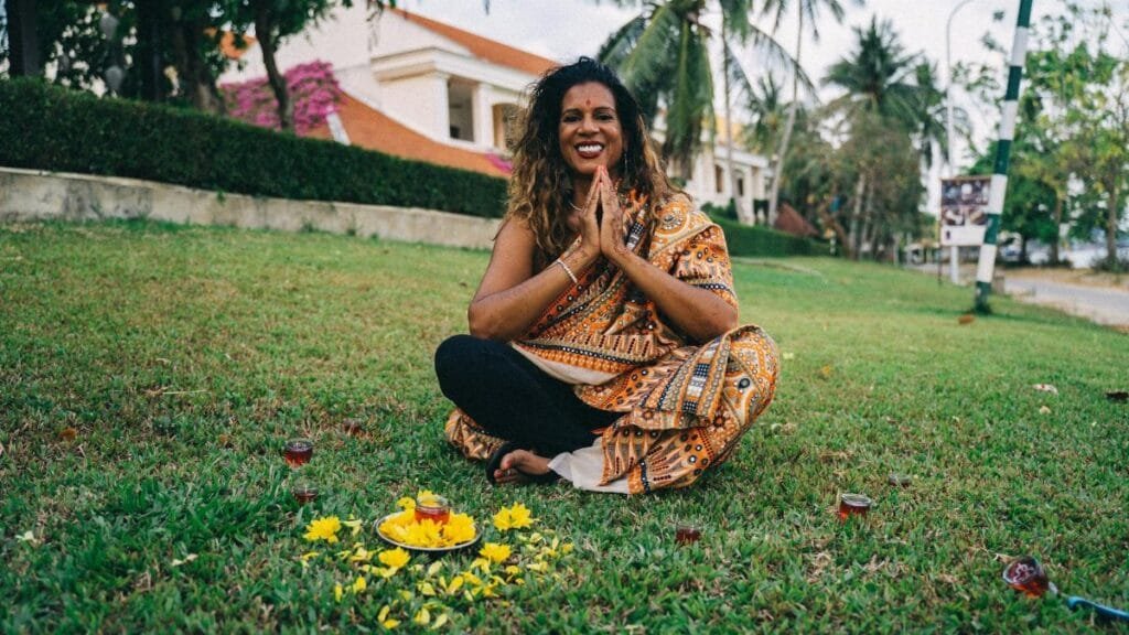 A smiling Indian woman in a saree participates in a traditional ritual outdoors, embracing cultural heritage.
