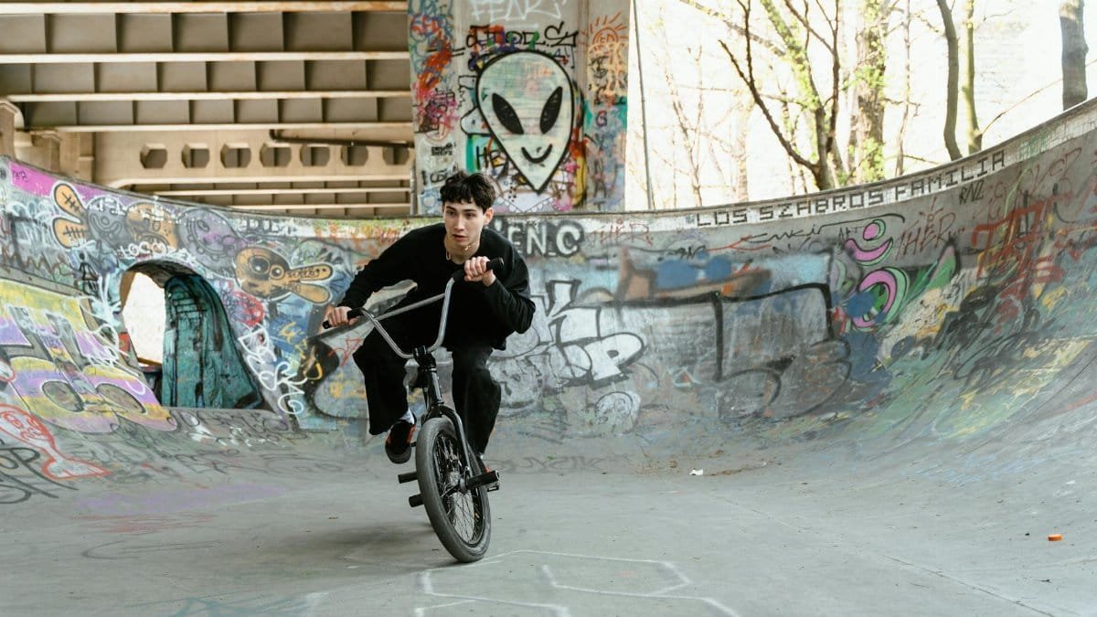 A young man performs a daring stunt on his BMX bike in a graffiti-covered skate park.