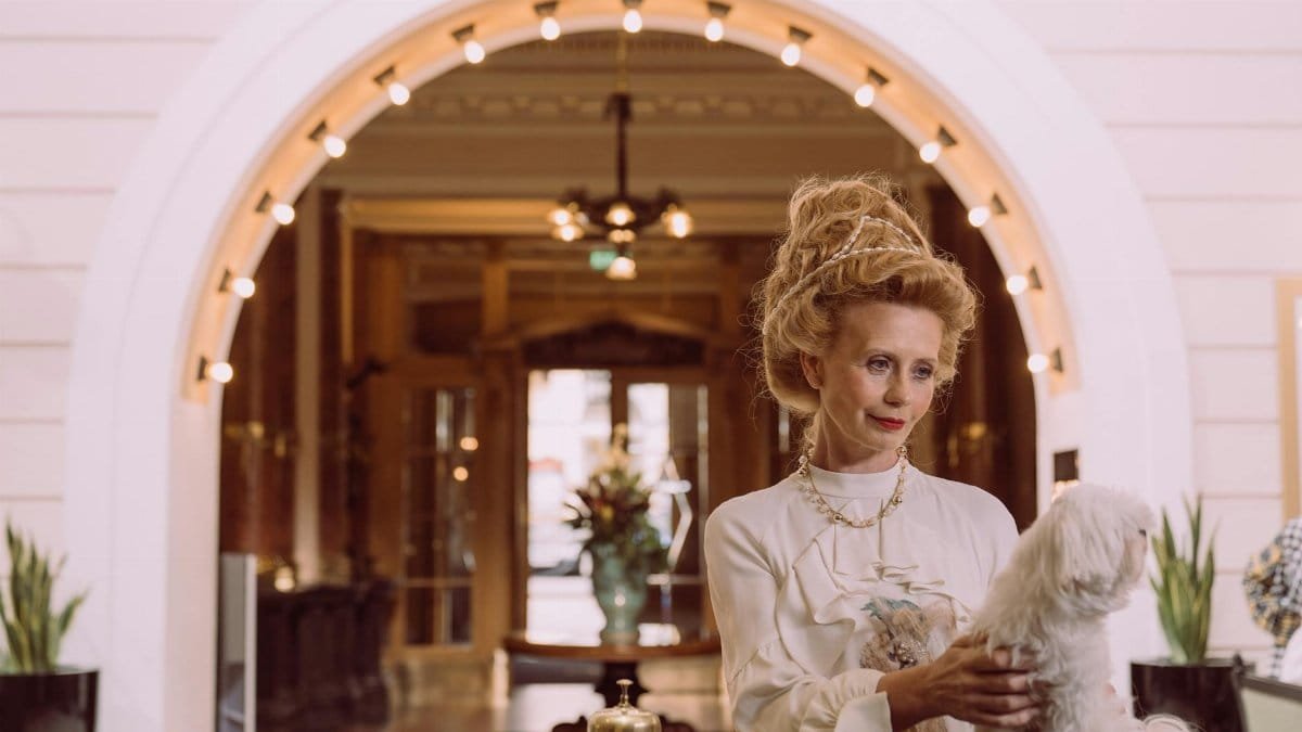 An elegant woman holding a dog at a luxurious hotel reception desk.