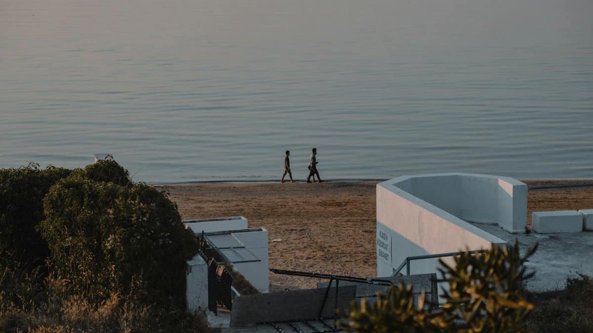 Two people walking along a tranquil beach with a view of the sea at dusk.