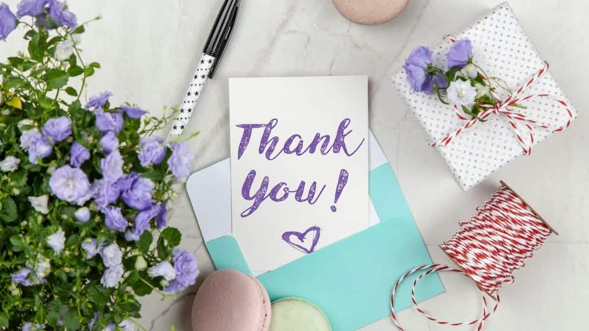 A beautifully arranged thank you card with lavender flowers, macarons, and gift package on a marble desk.