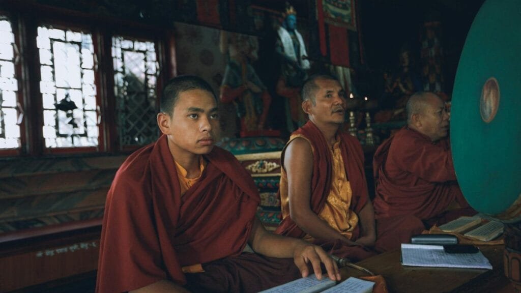 Three monks dressed in orange kasaya robes engaged in spiritual practice inside a buddhist temple.