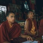 Three monks dressed in orange kasaya robes engaged in spiritual practice inside a buddhist temple.