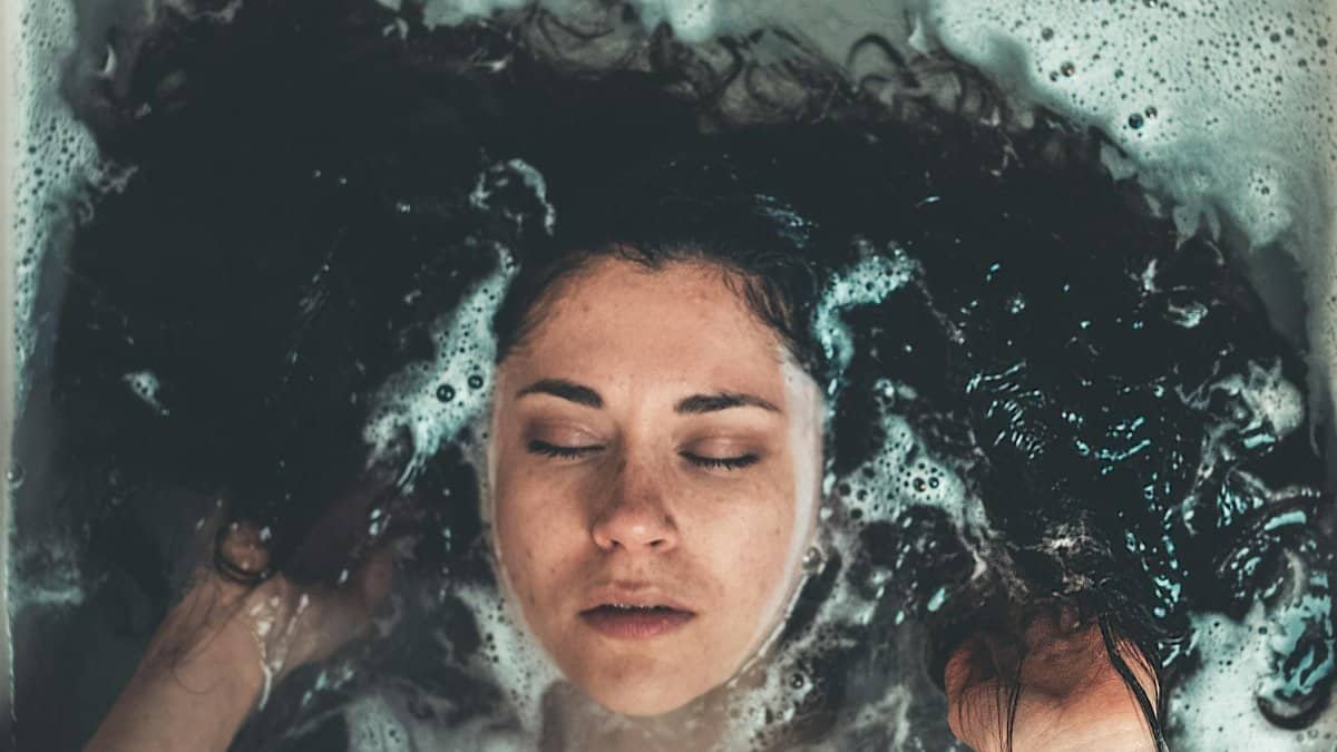 Close-up view of a woman meditating in a bathtub with eyes closed, immersed in a bubble bath.